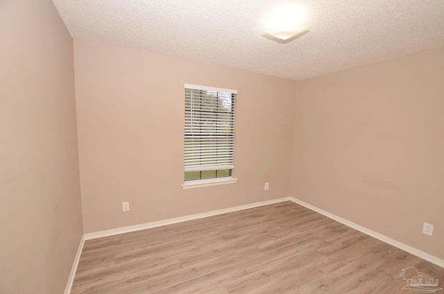 empty room with light wood-style flooring, baseboards, and a textured ceiling