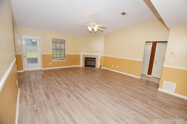 unfurnished living room featuring lofted ceiling, light wood-style floors, visible vents, and a tiled fireplace
