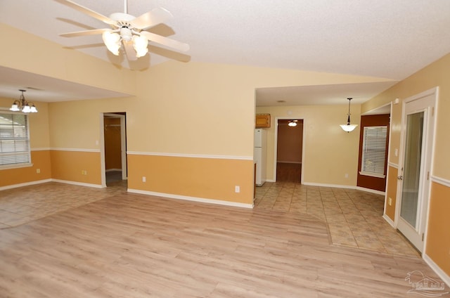 empty room with lofted ceiling, light wood finished floors, ceiling fan with notable chandelier, and baseboards
