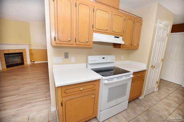 kitchen with a tile fireplace, under cabinet range hood, white electric range, open floor plan, and light countertops