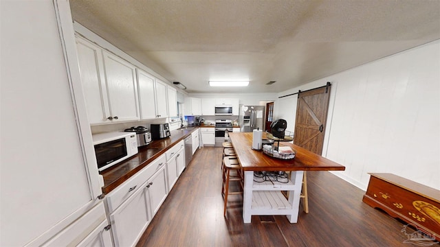 kitchen with a barn door, white cabinets, dark countertops, dark wood-type flooring, and stainless steel appliances