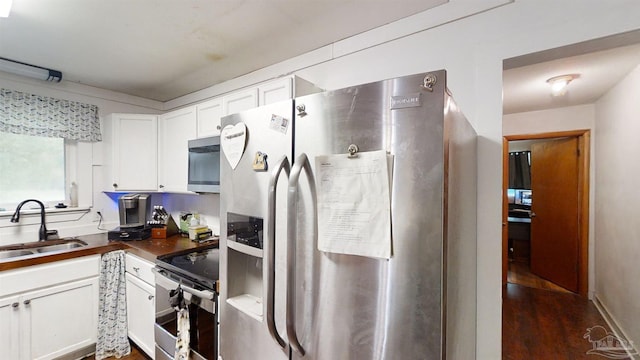 kitchen featuring stainless steel appliances, dark wood-style flooring, a sink, white cabinetry, and dark countertops