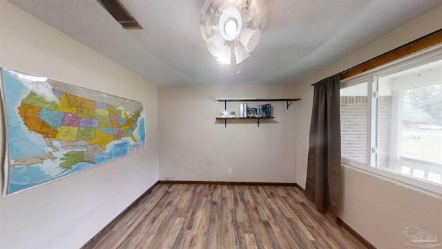 spare room with a textured ceiling, wood finished floors, visible vents, and baseboards