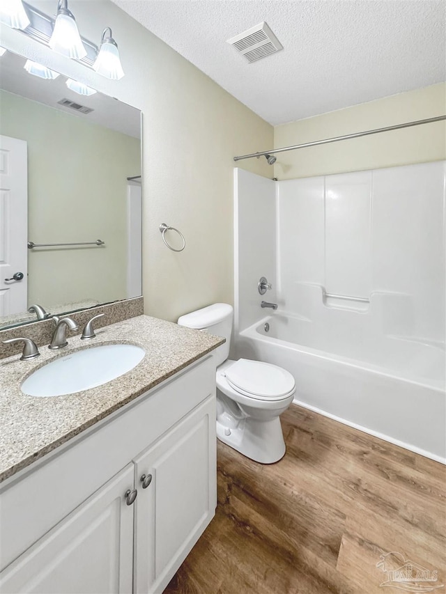 full bathroom with a textured ceiling, vanity, washtub / shower combination, hardwood / wood-style floors, and toilet