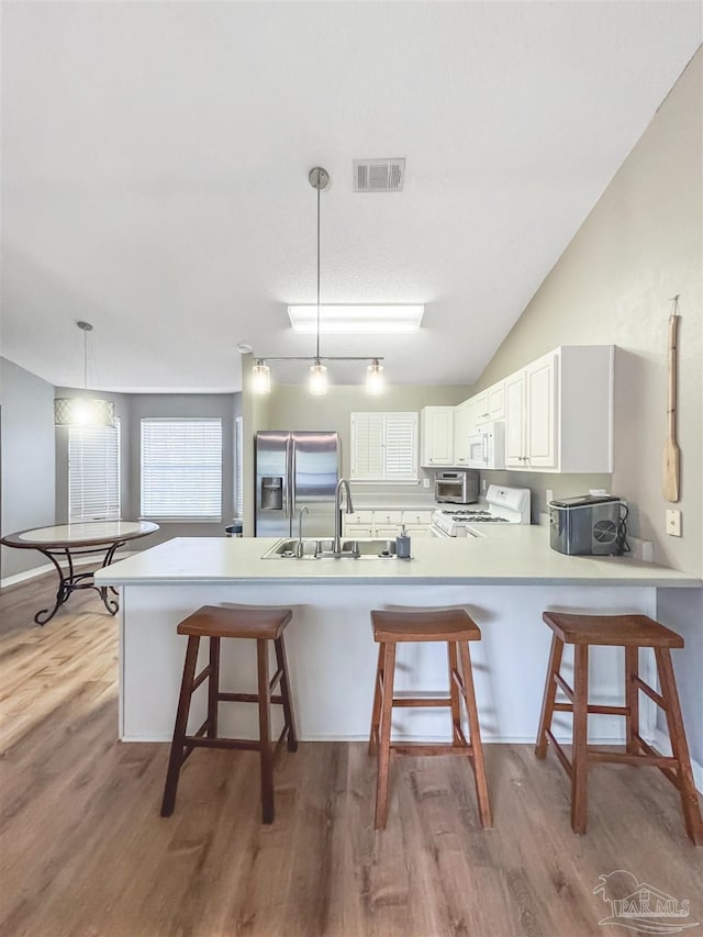 kitchen featuring a kitchen bar, white range oven, white cabinets, stainless steel fridge with ice dispenser, and hanging light fixtures