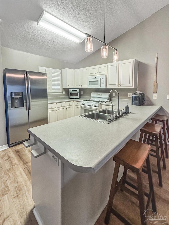 kitchen with kitchen peninsula, white appliances, vaulted ceiling, and a breakfast bar