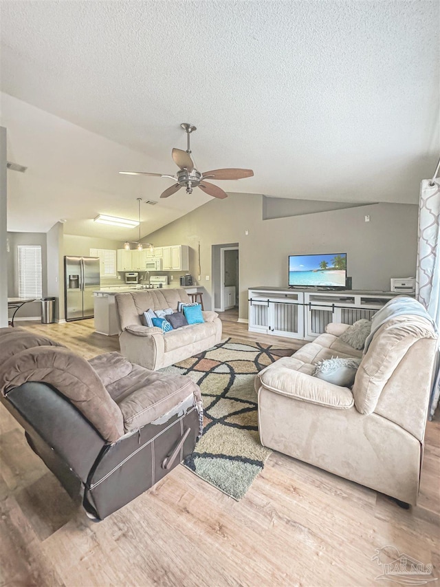 living room with ceiling fan, light hardwood / wood-style floors, lofted ceiling, and a textured ceiling