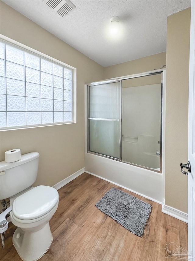 bathroom featuring hardwood / wood-style floors, a textured ceiling, toilet, and enclosed tub / shower combo