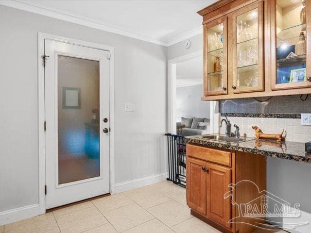 kitchen featuring sink, light tile patterned floors, dark stone countertops, ornamental molding, and backsplash