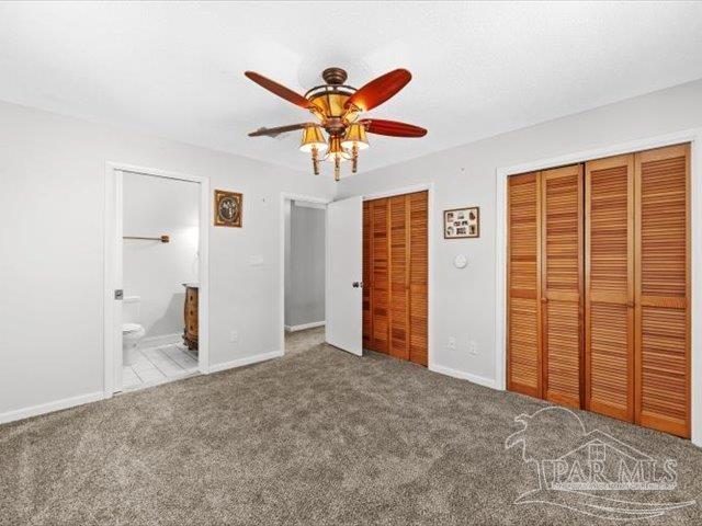 unfurnished bedroom featuring two closets, ensuite bathroom, ceiling fan, and carpet flooring