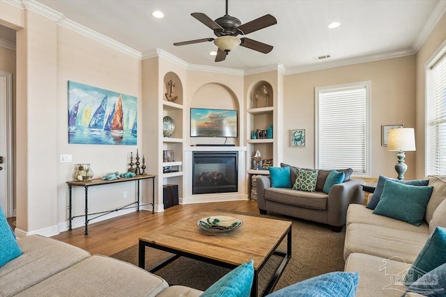 living room with crown molding, visible vents, wood finished floors, and a glass covered fireplace