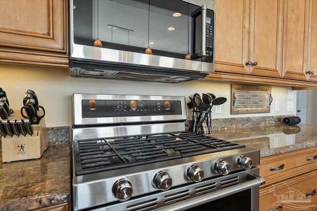 kitchen with dark stone counters, stainless steel appliances, and brown cabinets