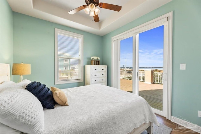 bedroom featuring access to outside, multiple windows, a tray ceiling, and baseboards