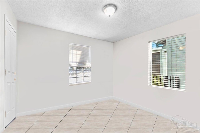 spare room featuring baseboards, a textured ceiling, and light tile patterned flooring