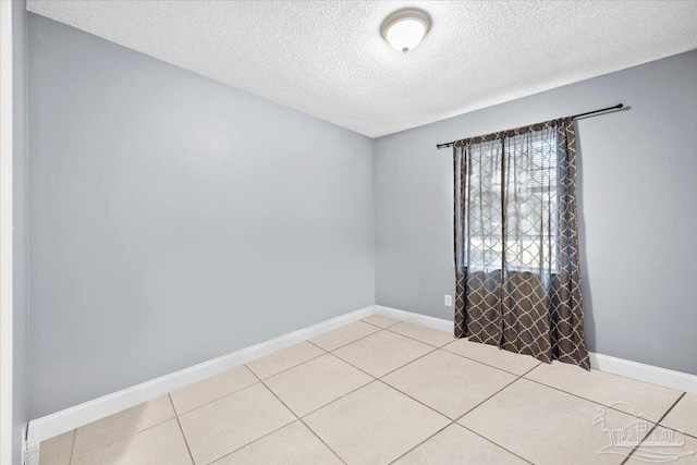 spare room featuring baseboards, a textured ceiling, and light tile patterned flooring