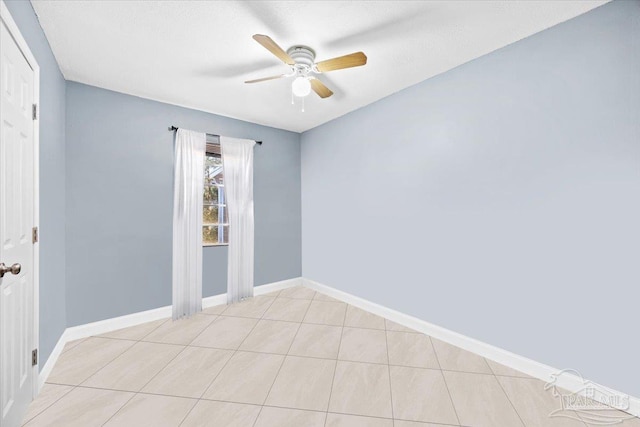 spare room featuring light tile patterned flooring, a ceiling fan, and baseboards