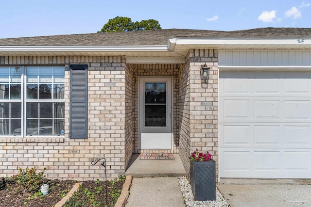 entrance to property with a garage, brick siding, and a shingled roof