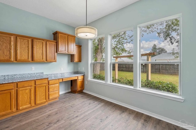 kitchen featuring hanging light fixtures, hardwood / wood-style flooring, built in desk, and light stone countertops