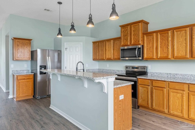 kitchen with light stone counters, appliances with stainless steel finishes, hanging light fixtures, and a center island with sink