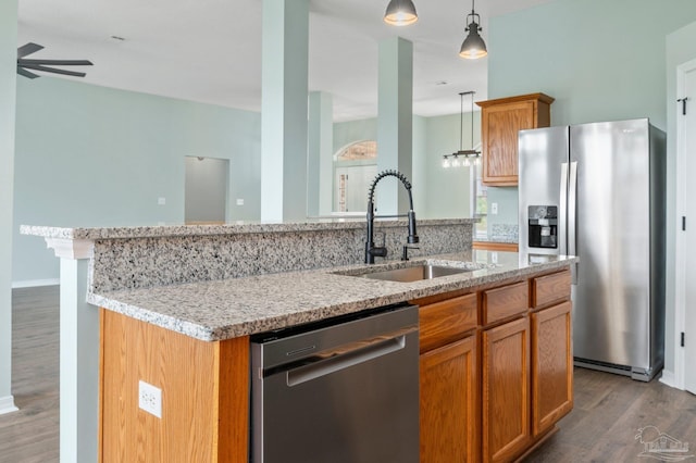 kitchen with appliances with stainless steel finishes, sink, light stone counters, and decorative light fixtures