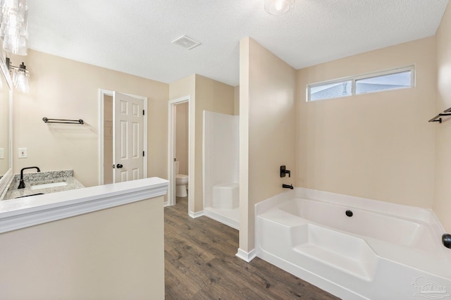 bathroom with wood-type flooring, vanity, a washtub, toilet, and a textured ceiling