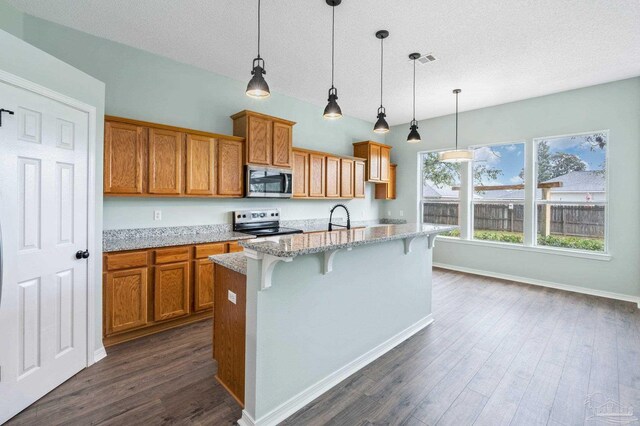 kitchen featuring a kitchen breakfast bar, dark hardwood / wood-style flooring, pendant lighting, stainless steel appliances, and a kitchen island with sink