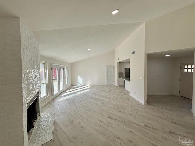 unfurnished living room with a brick fireplace, light wood-type flooring, and vaulted ceiling