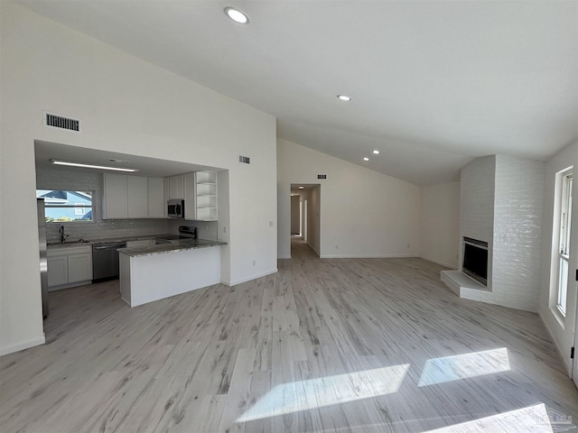 unfurnished living room featuring a large fireplace, sink, lofted ceiling, and light wood-type flooring