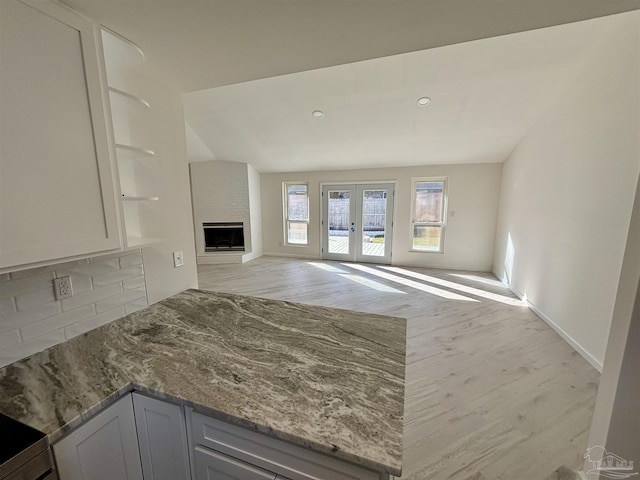 unfurnished living room featuring a large fireplace, light wood-type flooring, and french doors