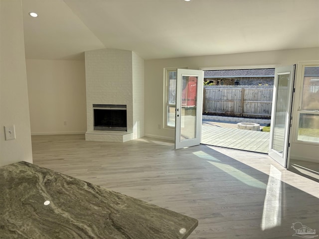 unfurnished living room featuring light wood-type flooring, a brick fireplace, and lofted ceiling