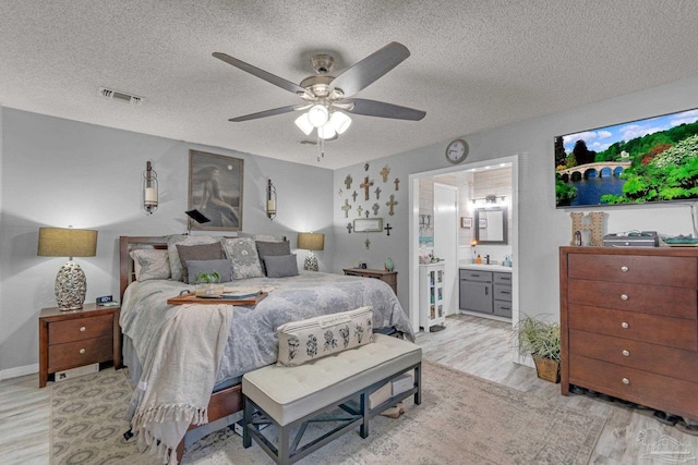 bedroom with connected bathroom, a textured ceiling, light hardwood / wood-style floors, and ceiling fan