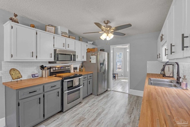 kitchen with appliances with stainless steel finishes, butcher block counters, sink, and gray cabinetry