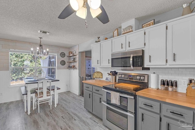 kitchen featuring butcher block countertops, white cabinetry, appliances with stainless steel finishes, pendant lighting, and backsplash