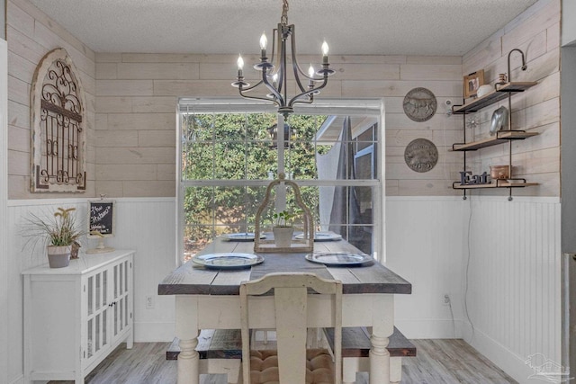 unfurnished dining area with wood walls, a textured ceiling, and light wood-type flooring