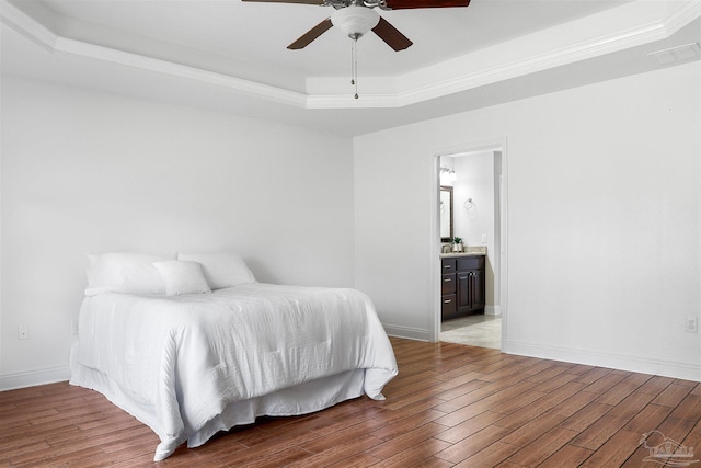 bedroom with connected bathroom, hardwood / wood-style flooring, a raised ceiling, and ceiling fan