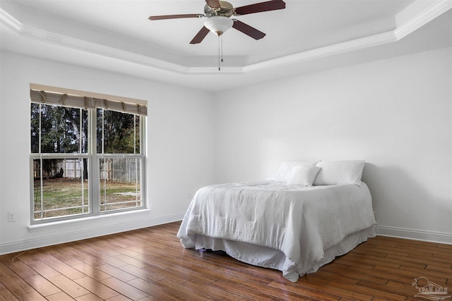 bedroom with a raised ceiling, dark wood-type flooring, and ceiling fan