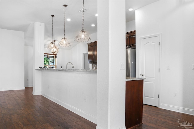 kitchen with stainless steel refrigerator, sink, hanging light fixtures, light stone countertops, and dark wood-type flooring