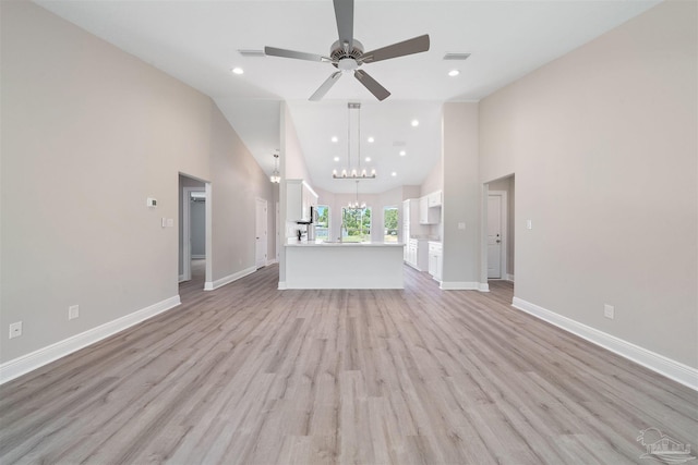 unfurnished living room with ceiling fan with notable chandelier, light wood-type flooring, and high vaulted ceiling