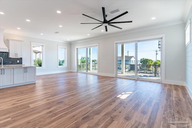 unfurnished living room with dark hardwood / wood-style flooring, ornamental molding, sink, and ceiling fan