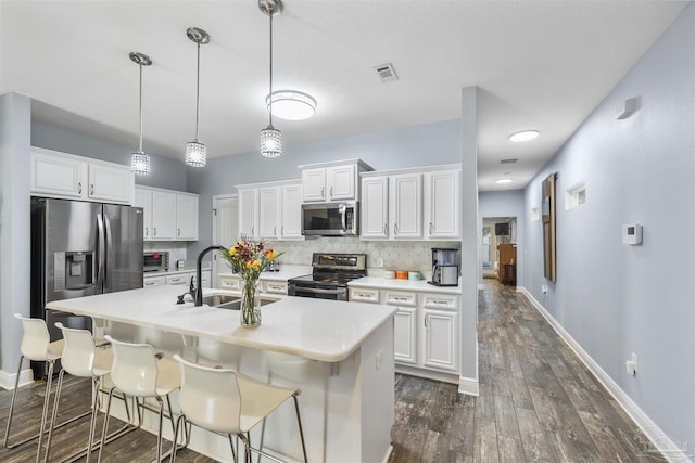kitchen with appliances with stainless steel finishes, a sink, dark wood-style floors, light countertops, and white cabinetry