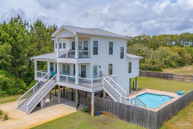 back of house with stairway, a fenced backyard, a balcony, a yard, and metal roof
