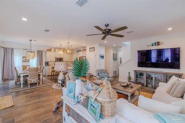 living room featuring ornamental molding, ceiling fan with notable chandelier, and visible vents