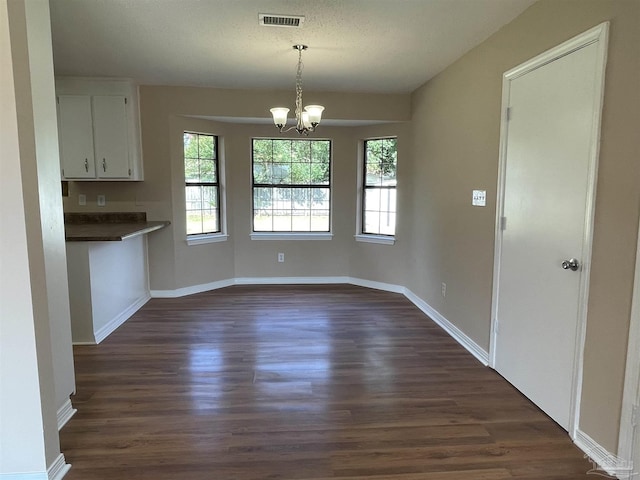 unfurnished dining area with dark hardwood / wood-style floors, a notable chandelier, and a textured ceiling