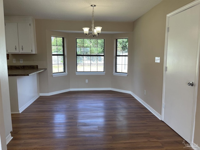 unfurnished dining area featuring dark hardwood / wood-style floors, a textured ceiling, and an inviting chandelier