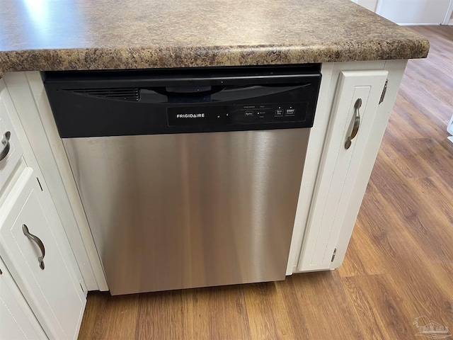 interior details with stainless steel dishwasher, light hardwood / wood-style flooring, and white cabinets