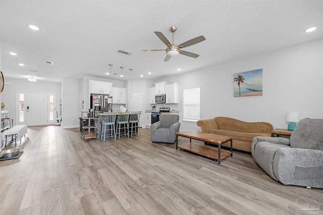 living room with ceiling fan, light wood-type flooring, and a textured ceiling