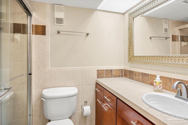 bathroom featuring a shower with shower door, vanity, tasteful backsplash, tile walls, and toilet