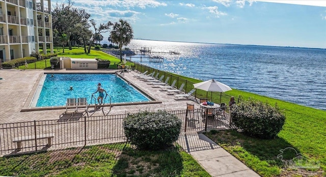 community pool with a patio area, fence, a yard, and a water view