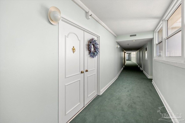 corridor featuring a textured ceiling, a healthy amount of sunlight, and dark carpet