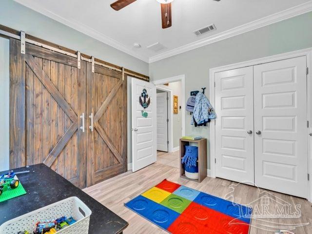 1516 Cadence Loop, Cantonment, FL 32533 - game room with wood finished floors, a barn door, ornamental molding, and a ceiling fan